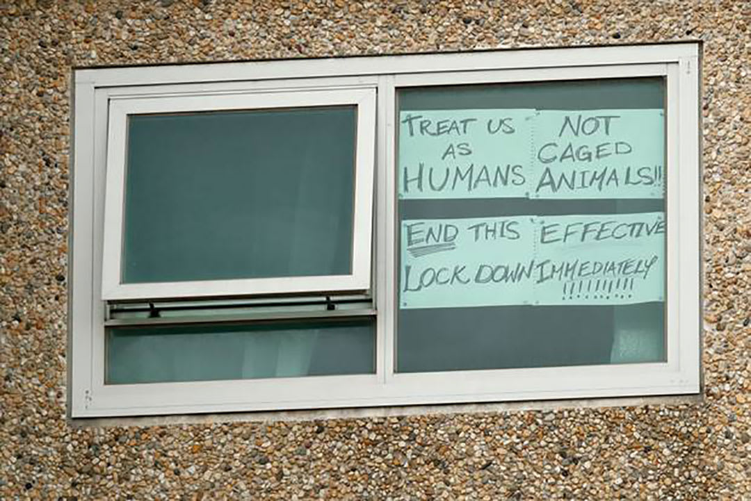 Pic of window in Melbourne public housing tower with signs protesting the COVID lockdown