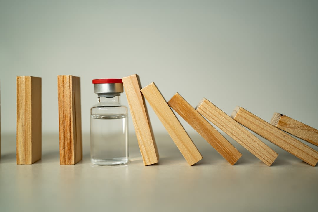 A medicine vial sits between a row of wooden blocks, stopping a domino effect.