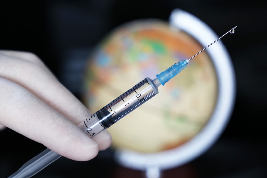 A globe of the world and a person holding a syringe.