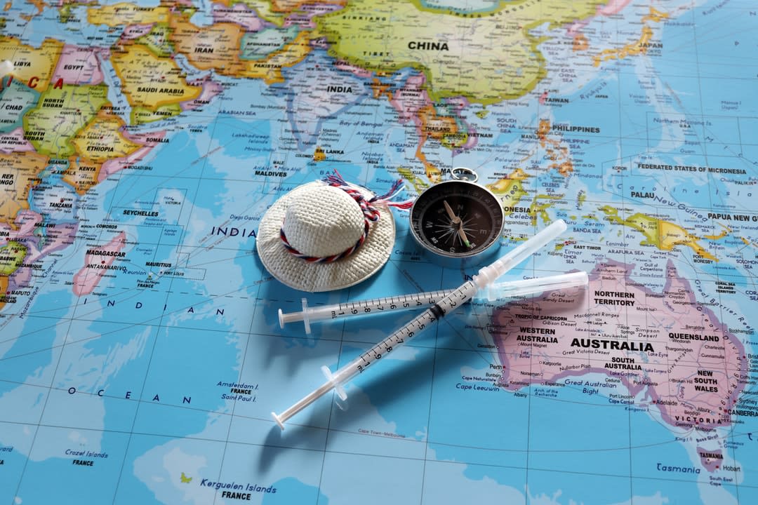 A compass, sunhat and two syringes on a map of the world.