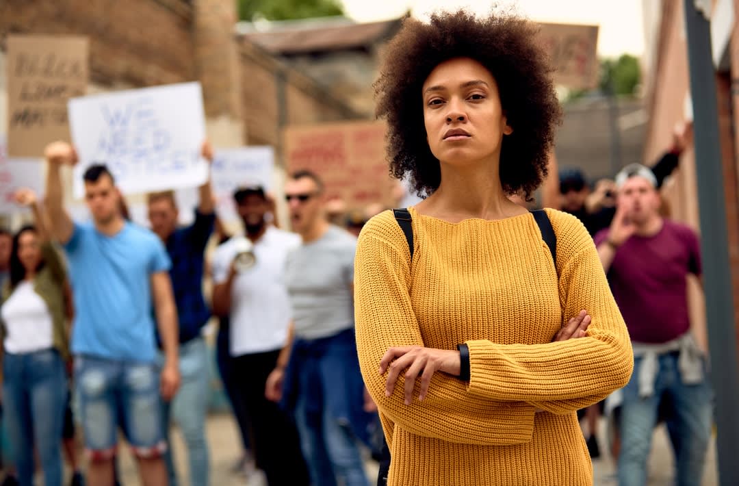 A defiant woman stands in front of a group of men holding up placards calling for justice. 