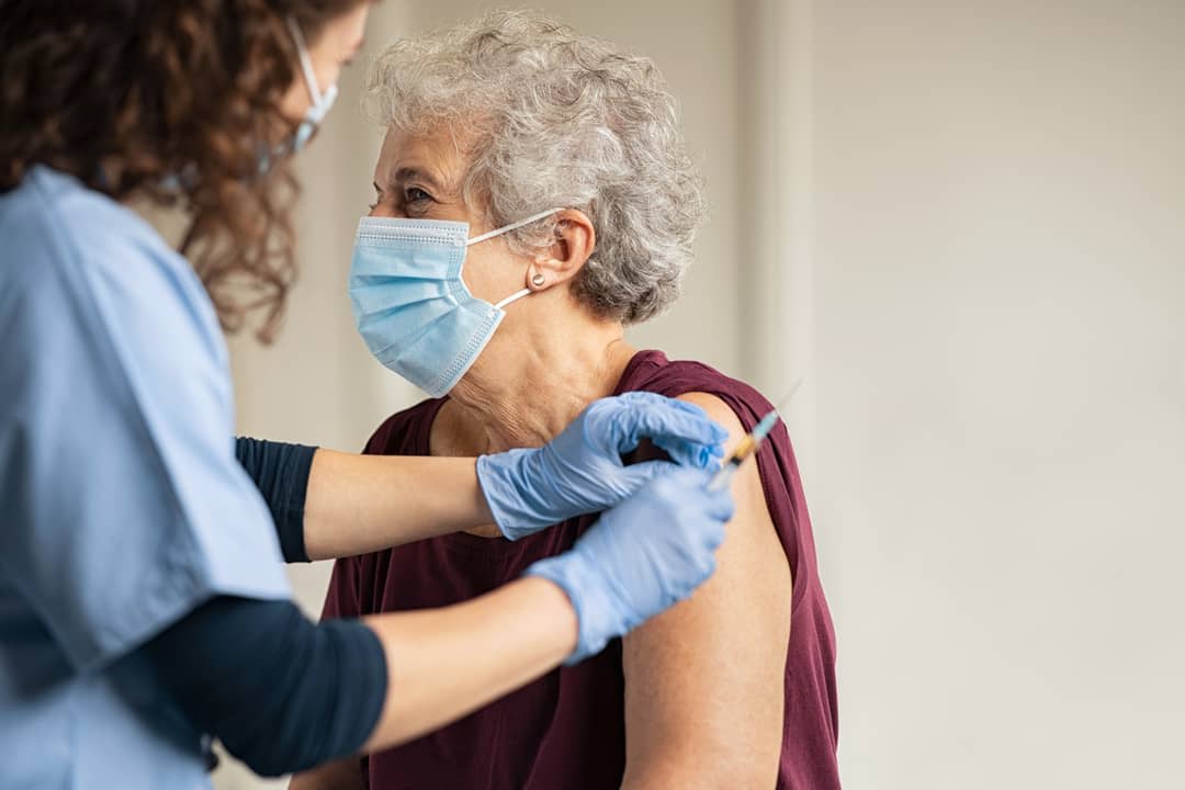 General practitioner vaccinating old patient in private clinic