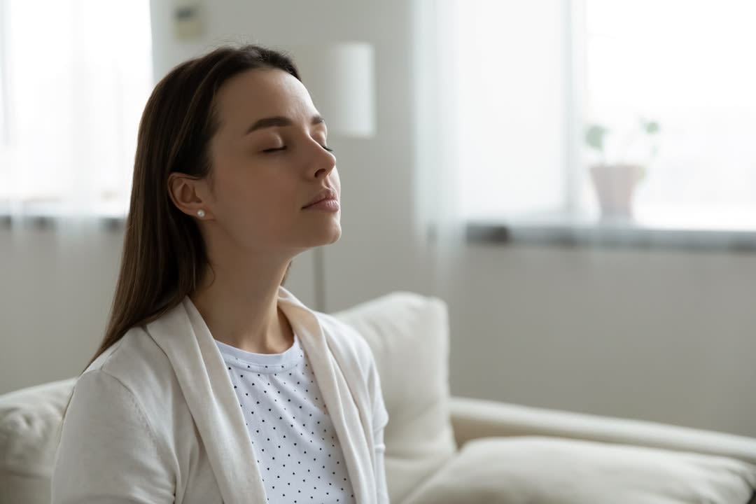 A woman sits on a couch breathing clean air.