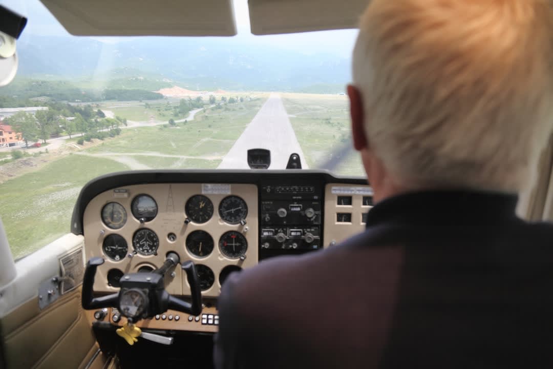 An old man in a cockpit, sitting at the controls of a plane.