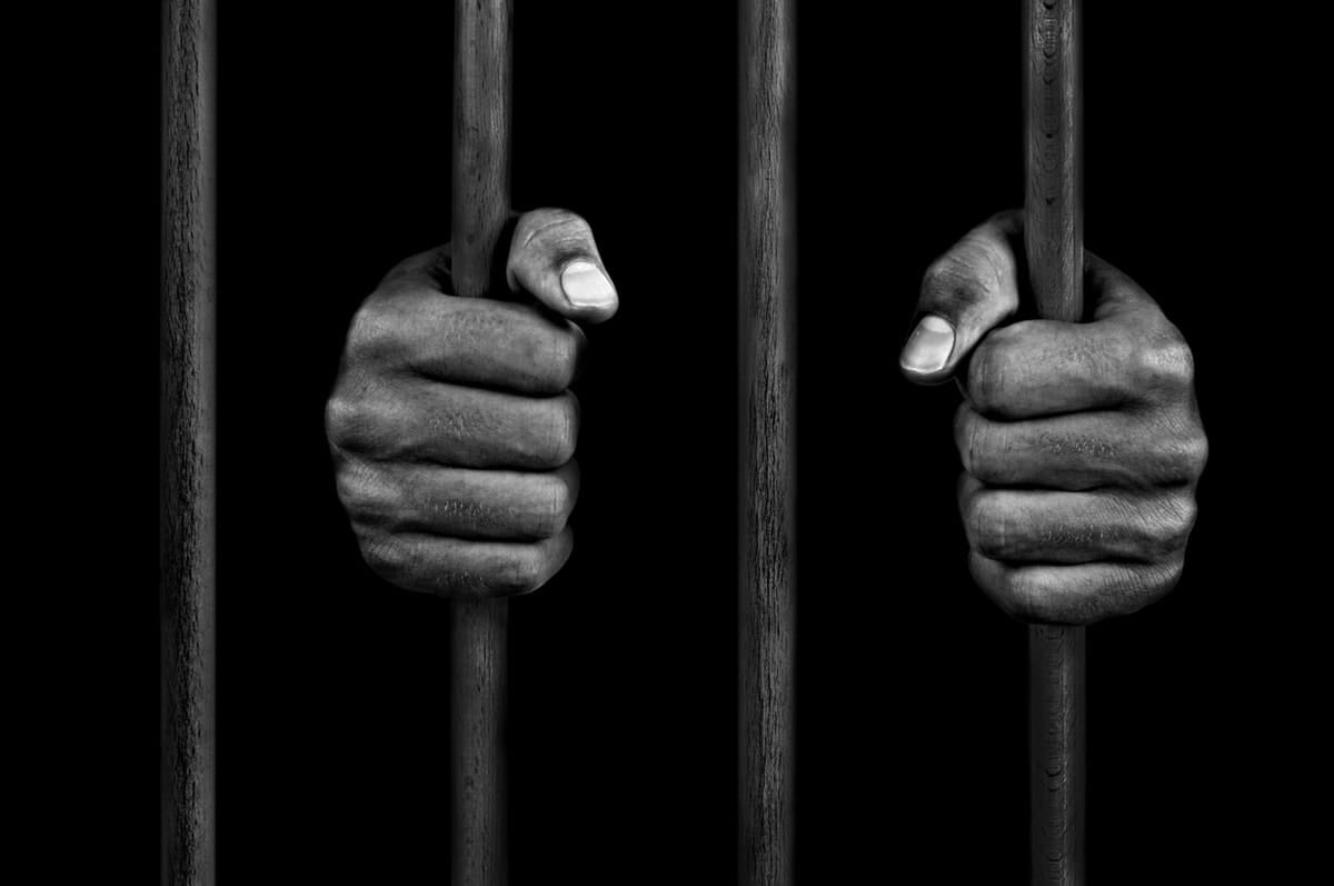 Monochrome image of hands holding prison bars