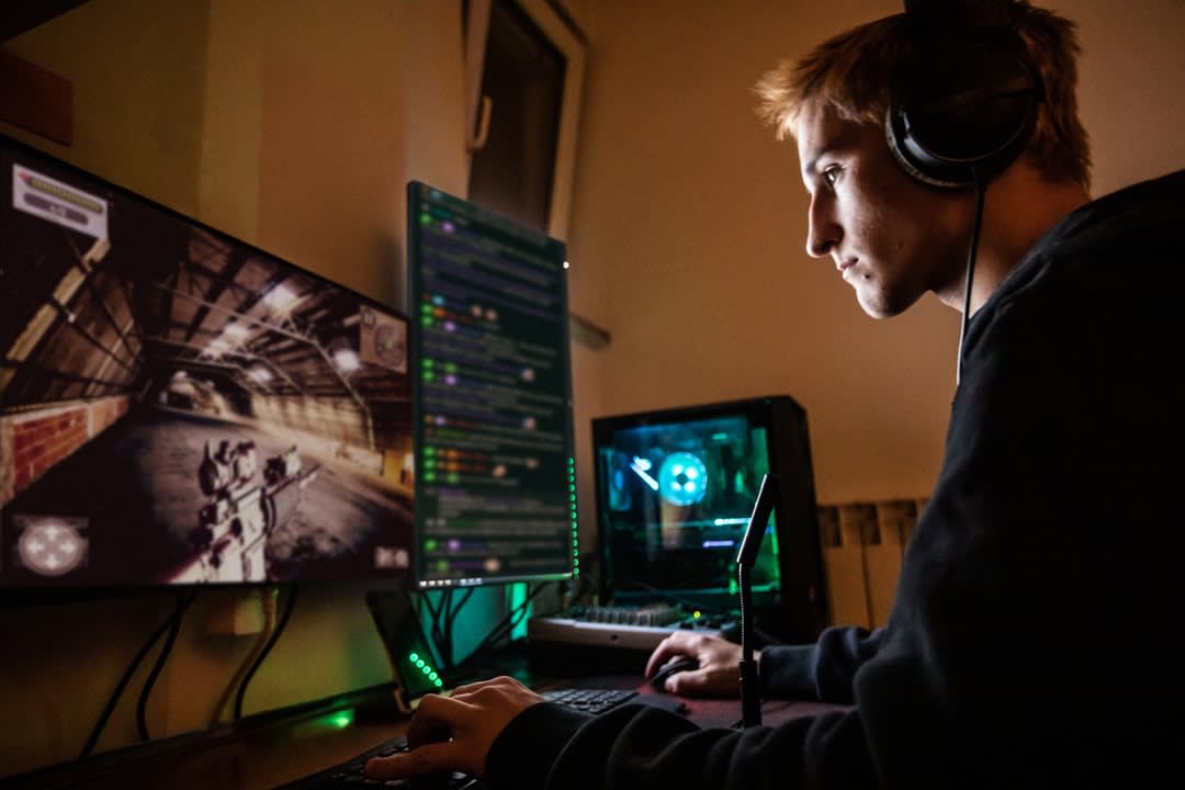 A young man sits in front of multiple screens playing video games.