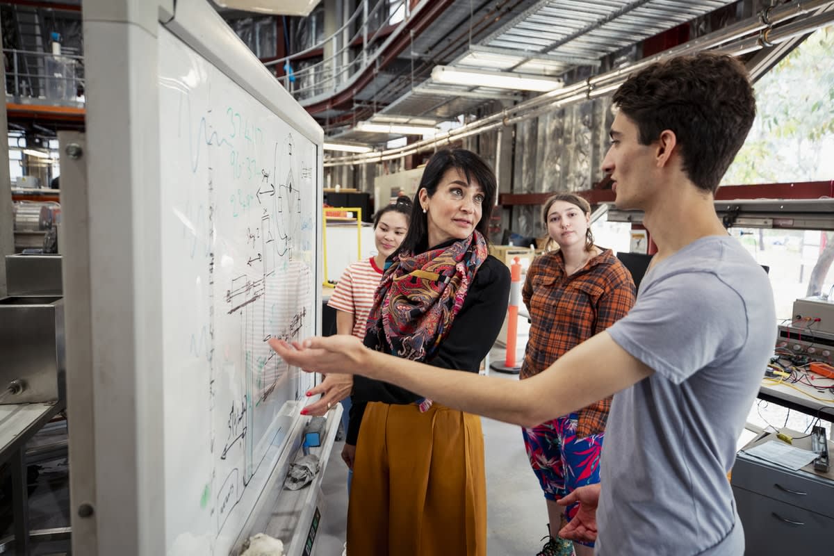 A teacher and students discussing material on a whiteboard in a lab setting