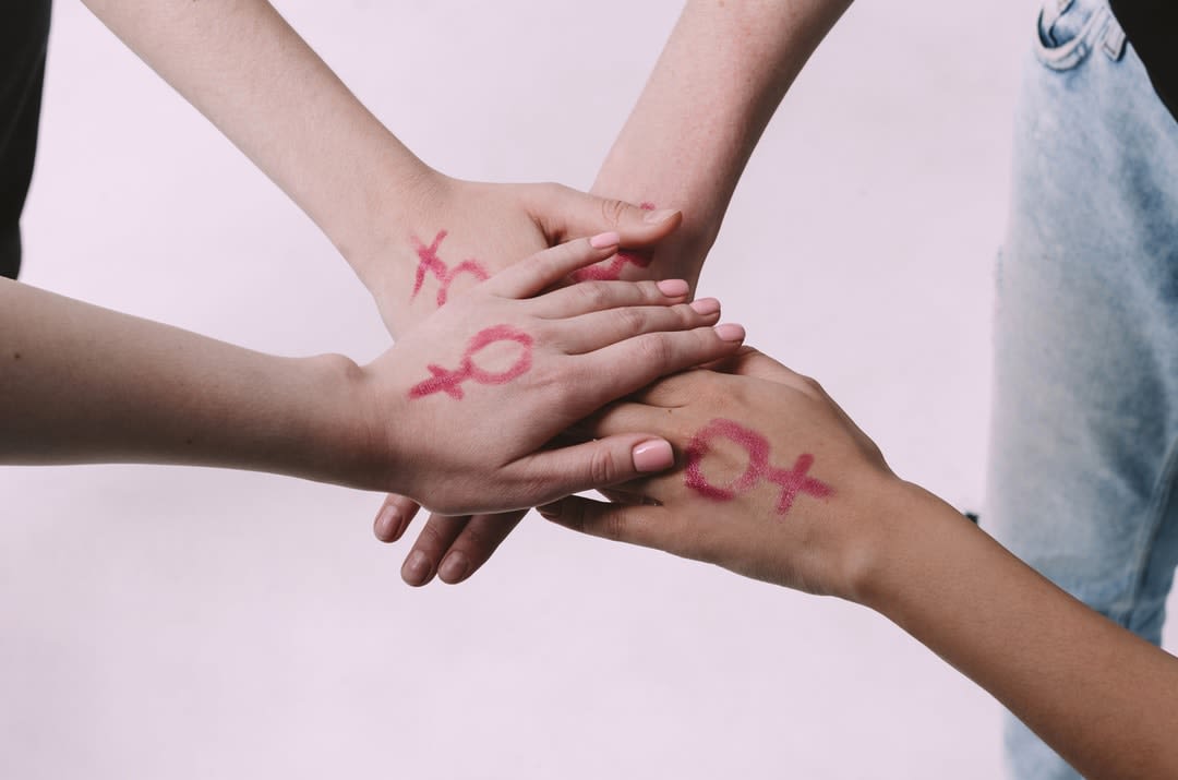 Four women join hands with the femaile gender symbol painted on the back of their hands.