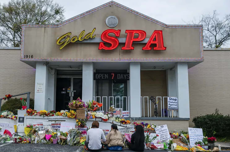 Three mourners sit amid the floral tributes outside Gold Spa, the scene of two of the massage parlour shootings in Atlanta, Georgia.