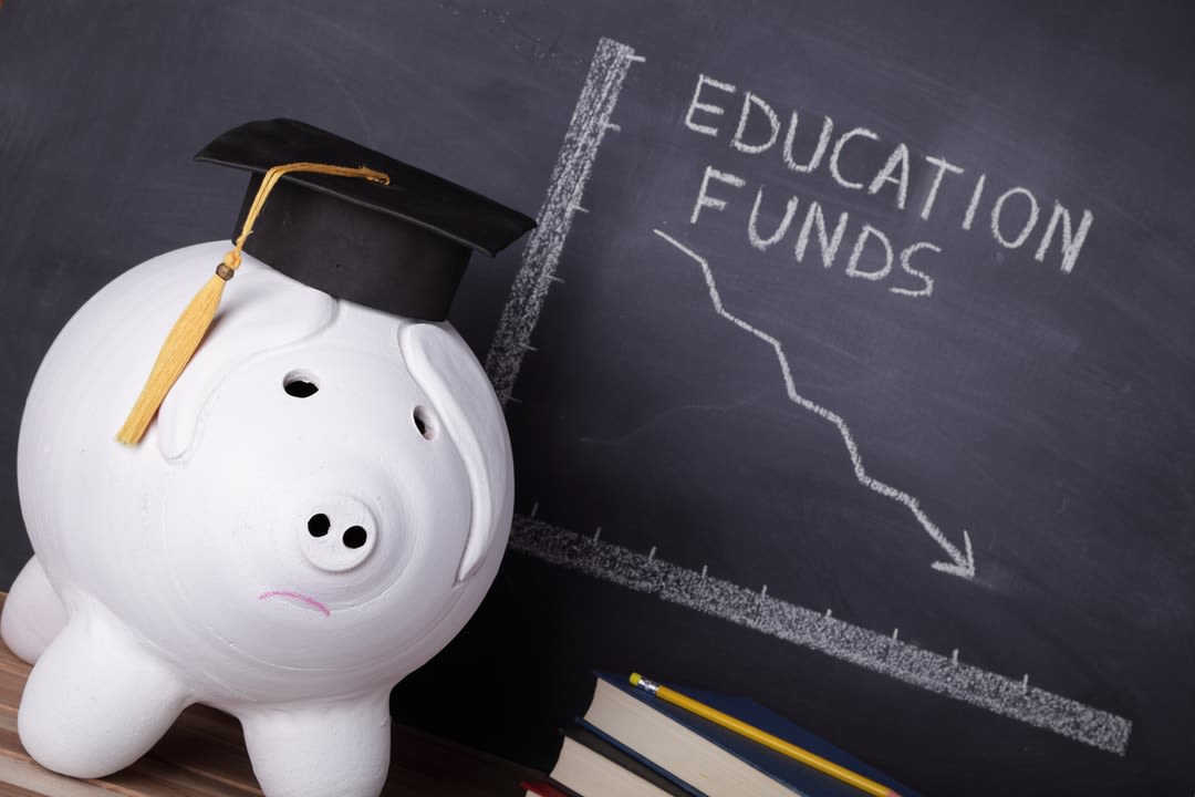 A piggy bank with a blackboard in the background showing diminishing funds.