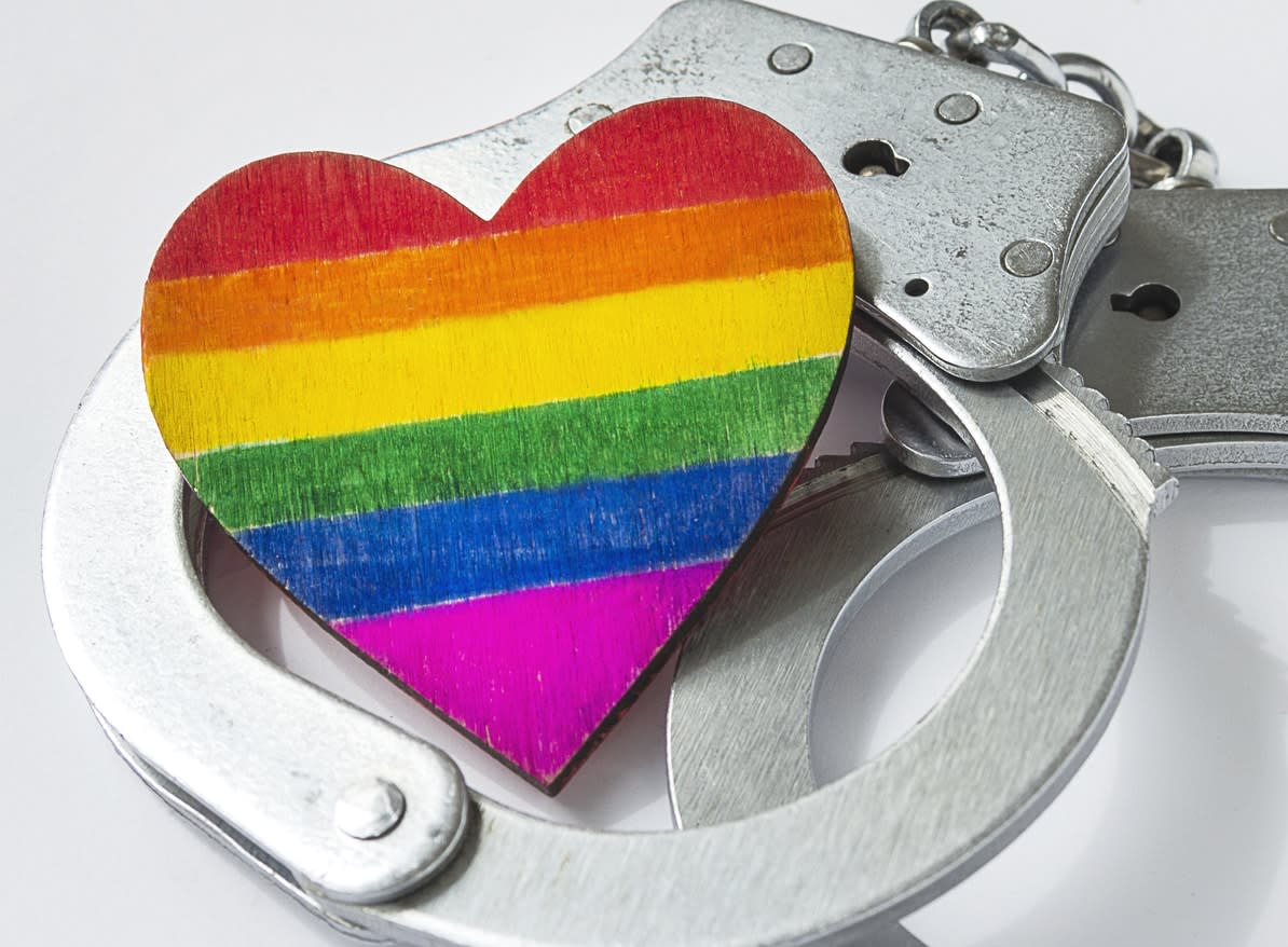 A wooden love heart painted in LGBTQ colours, sitting on a pair of handcuffs