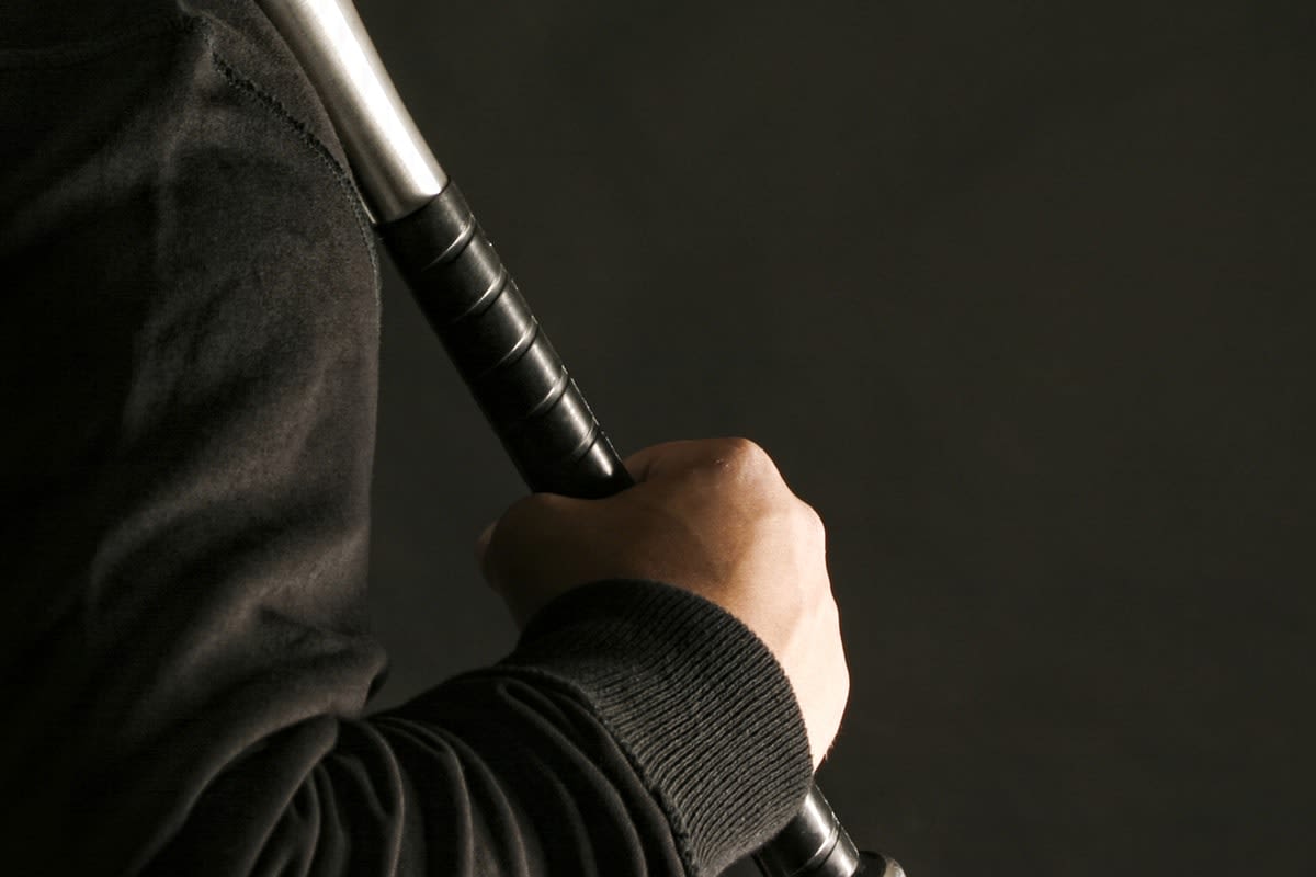 Close-up of a man's hand holding a baseball bat in a threatening manner 