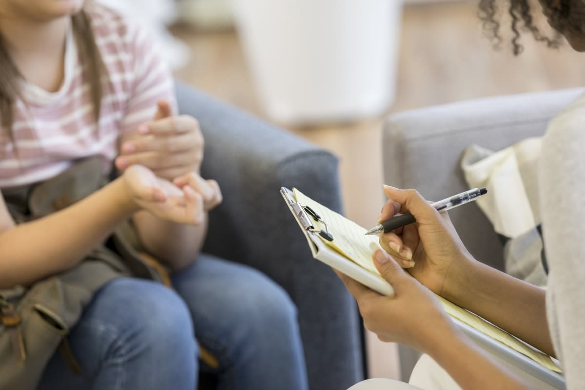 A woman taking notes while talking to a child - faces unseen