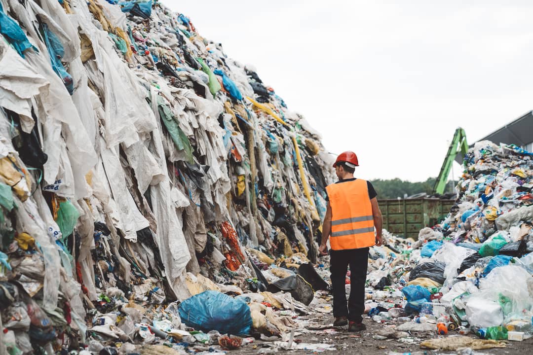 A workman walks between piles of discarded clothing.