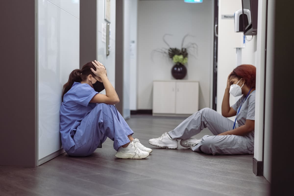 Two exhausted and distressed female nurses, sitting on the floor with heads in hands