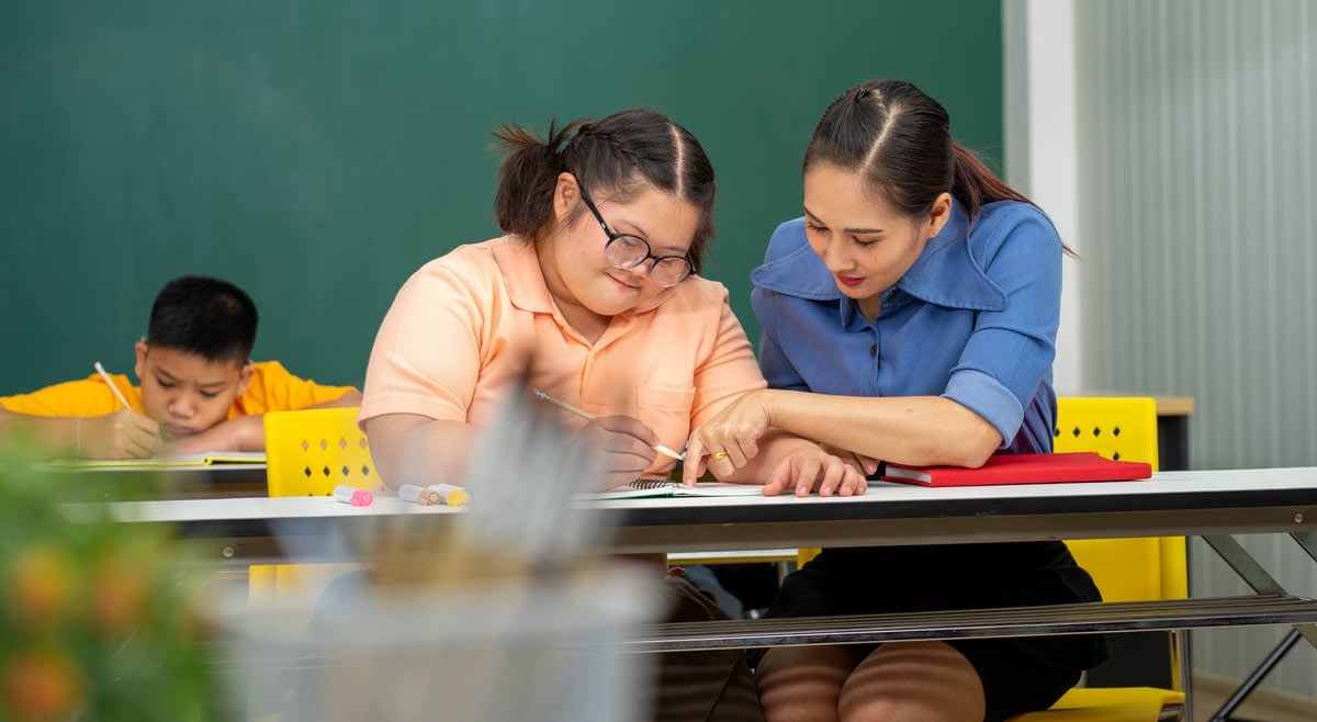 A female teacher assisting a disabled girl with her schoolwork in a classroom