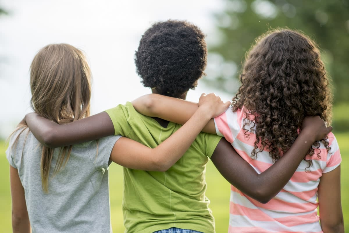 Three children photographed from behind, with their arms around each other’s back