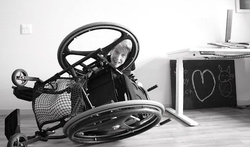 A smiling Dr Melinda Smith looking through a hole in her overturned wheelchair - black and white image
