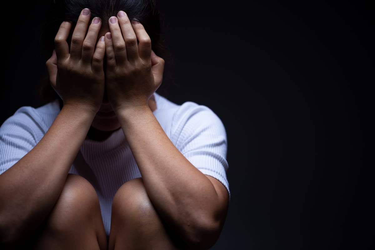 Indigenous woman with her head in her hands against a black background.