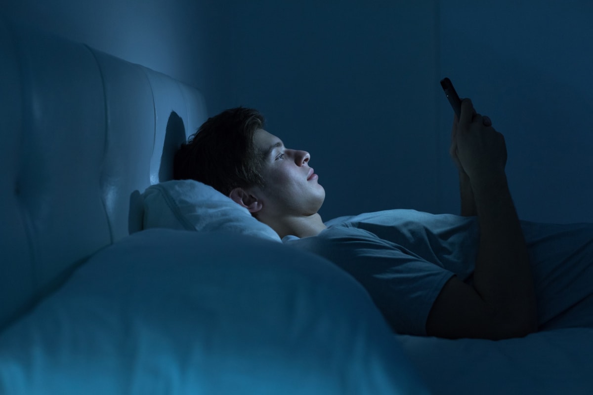 Man lying in bed at night looking at his mobile phone.