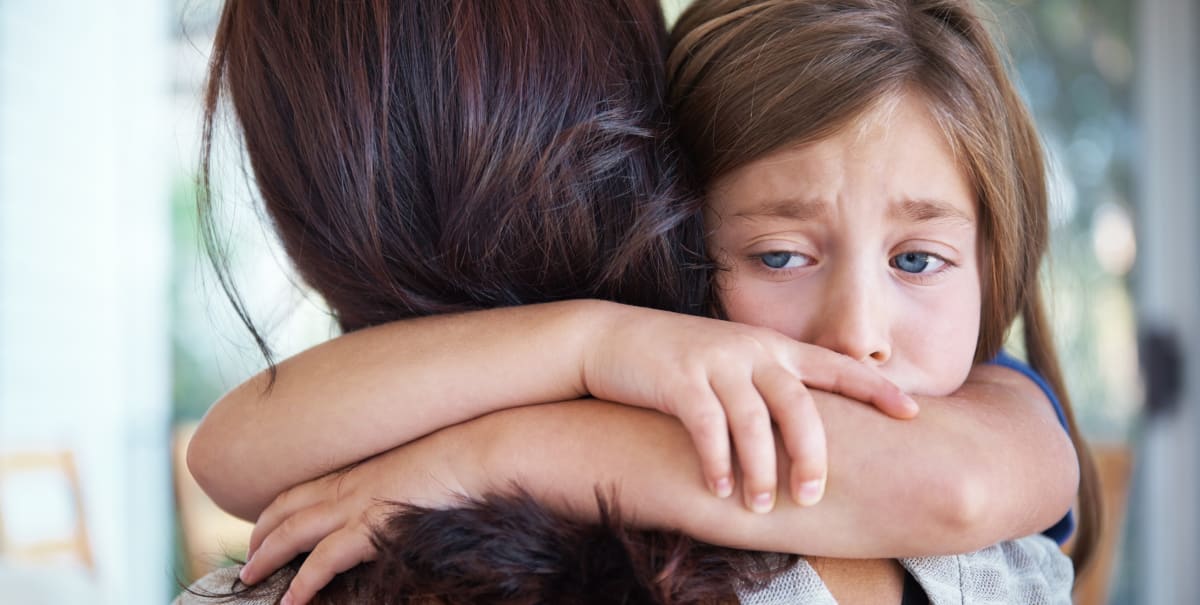 Closeup shot of a crying little girl hugging her mom around her neck