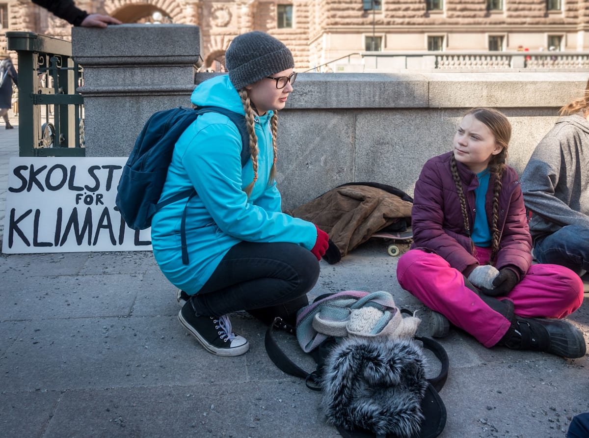 Greta Thunberg sitting looking at another young woman activist in the school strike for the climate outside the Swedish parliament in April 2019.