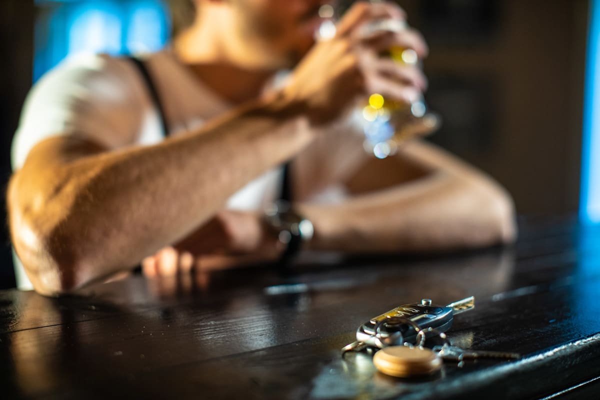 Blurred man sitting at a bar drinking, with car key on the bar in the foreground