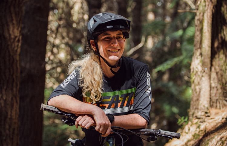 Mountainbike rider Kate Weatherly on a forest trail, leaning on her bike and smiling.