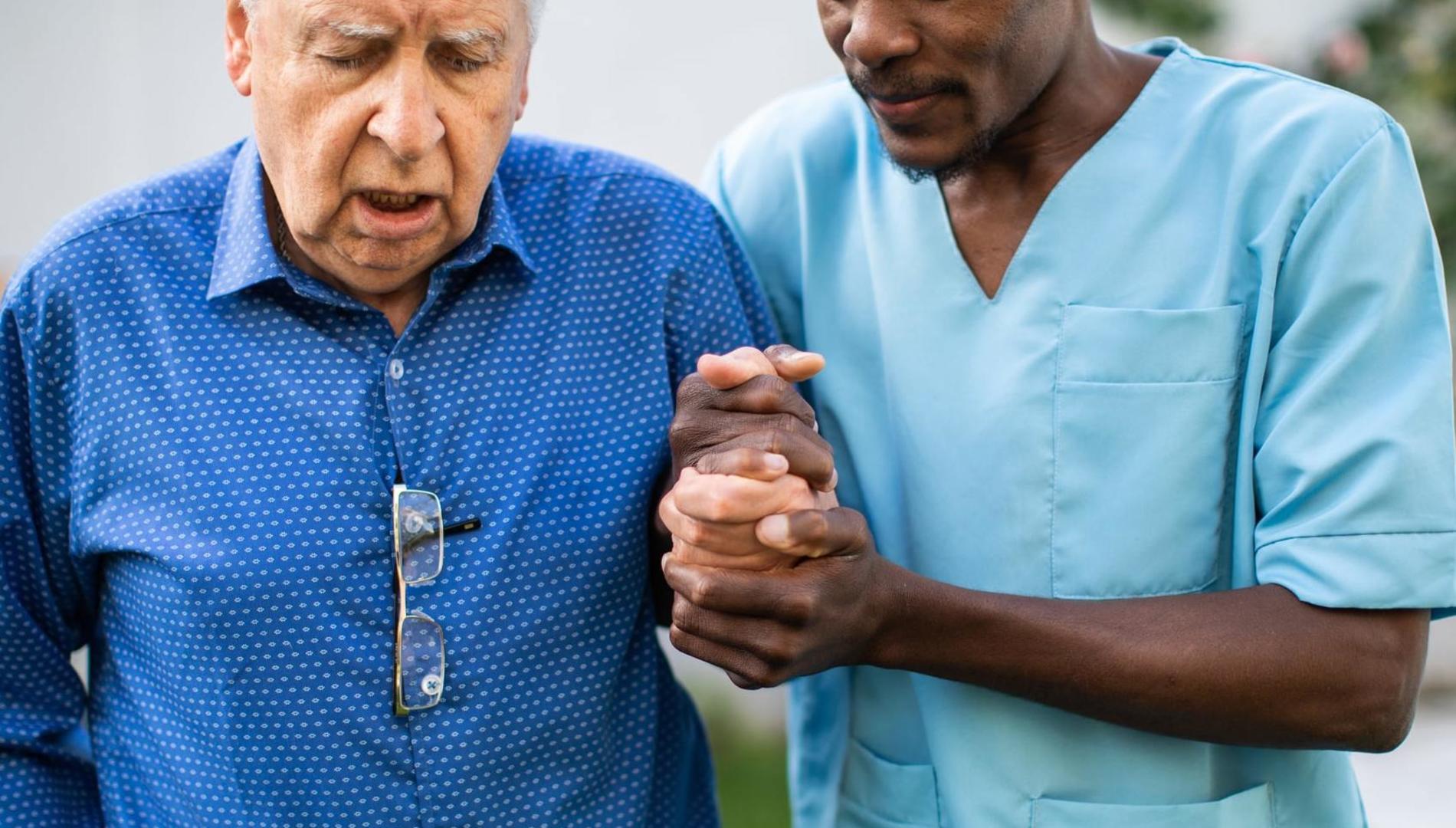 Black male nurse assisting senior man to walk outdoors