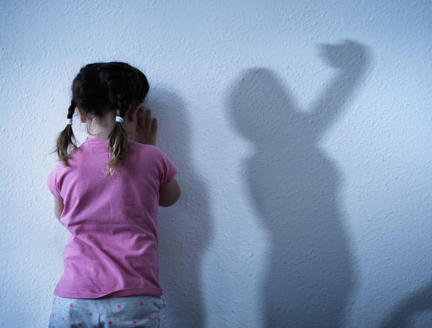 Girl facing a wall while shadows of parents are fighting