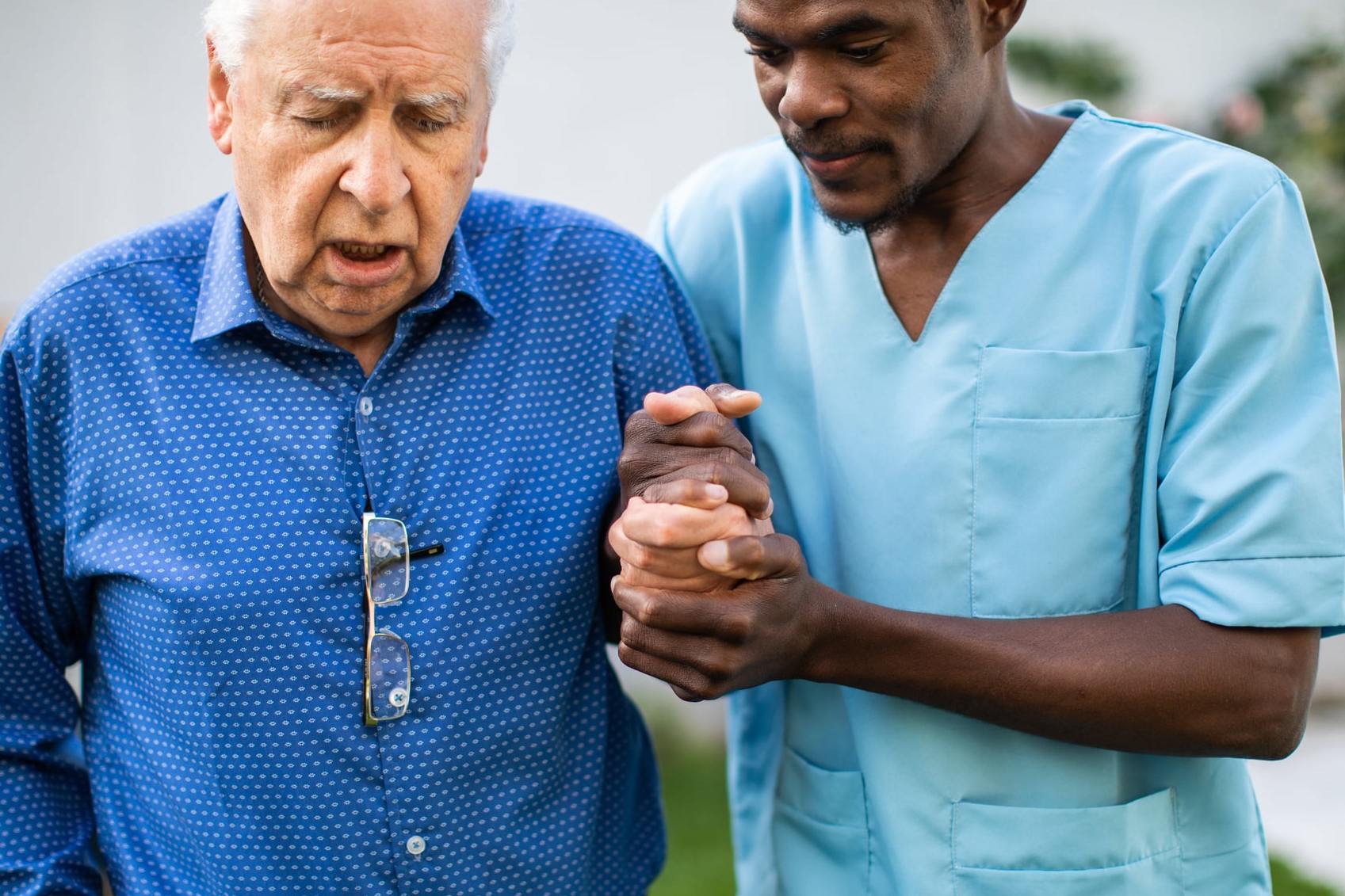 Black male nurse assisting senior man to walk outdoors