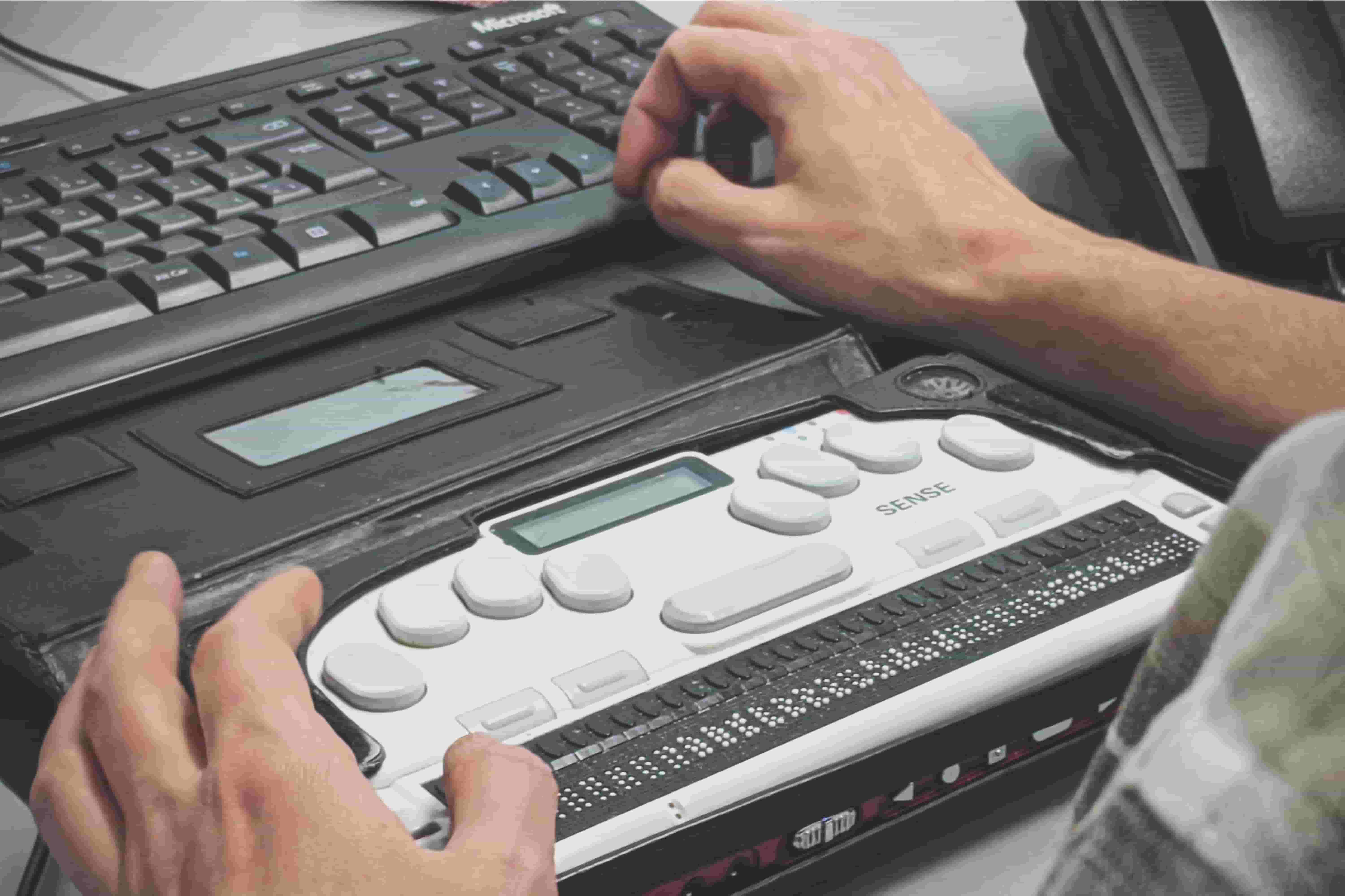 A user sitting in front of a computer using a Braille reader.