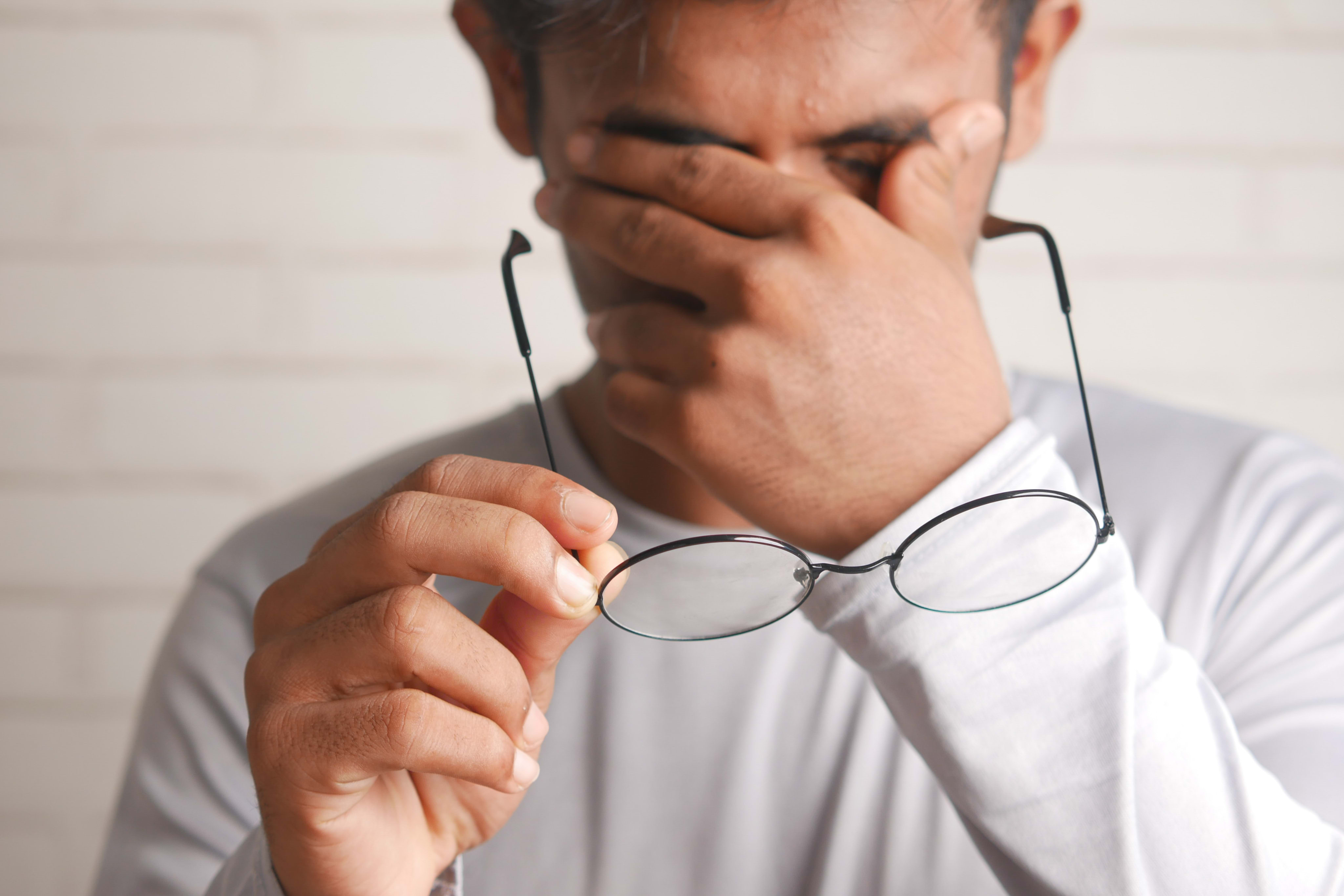 A man holding his glasses in his hands while rubbing the bridge of his nose in frustration.