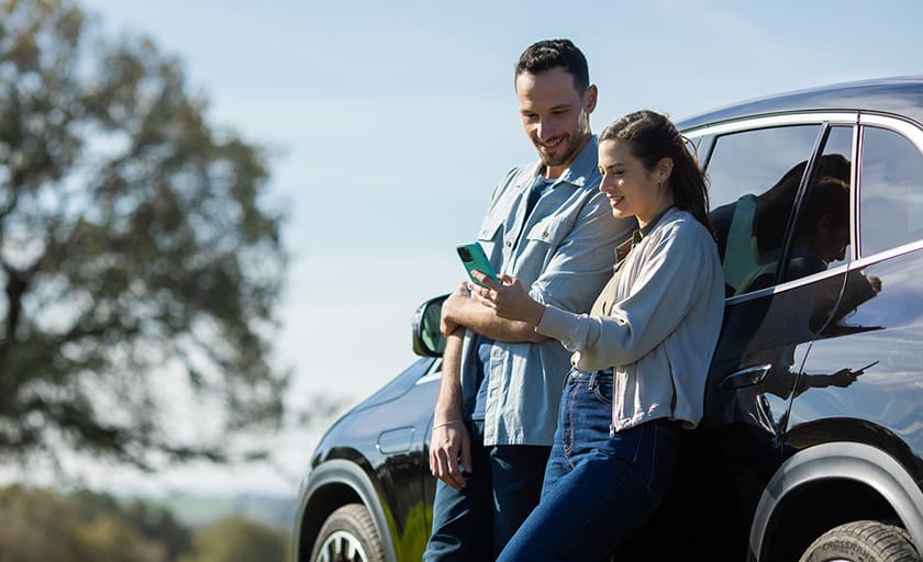 גבר ואישה נשענים על רכב ומסתכלים בטלפון נייד