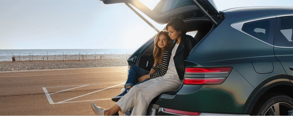 אישה וילדה יושבים בתא המטען של רכב לצד הים