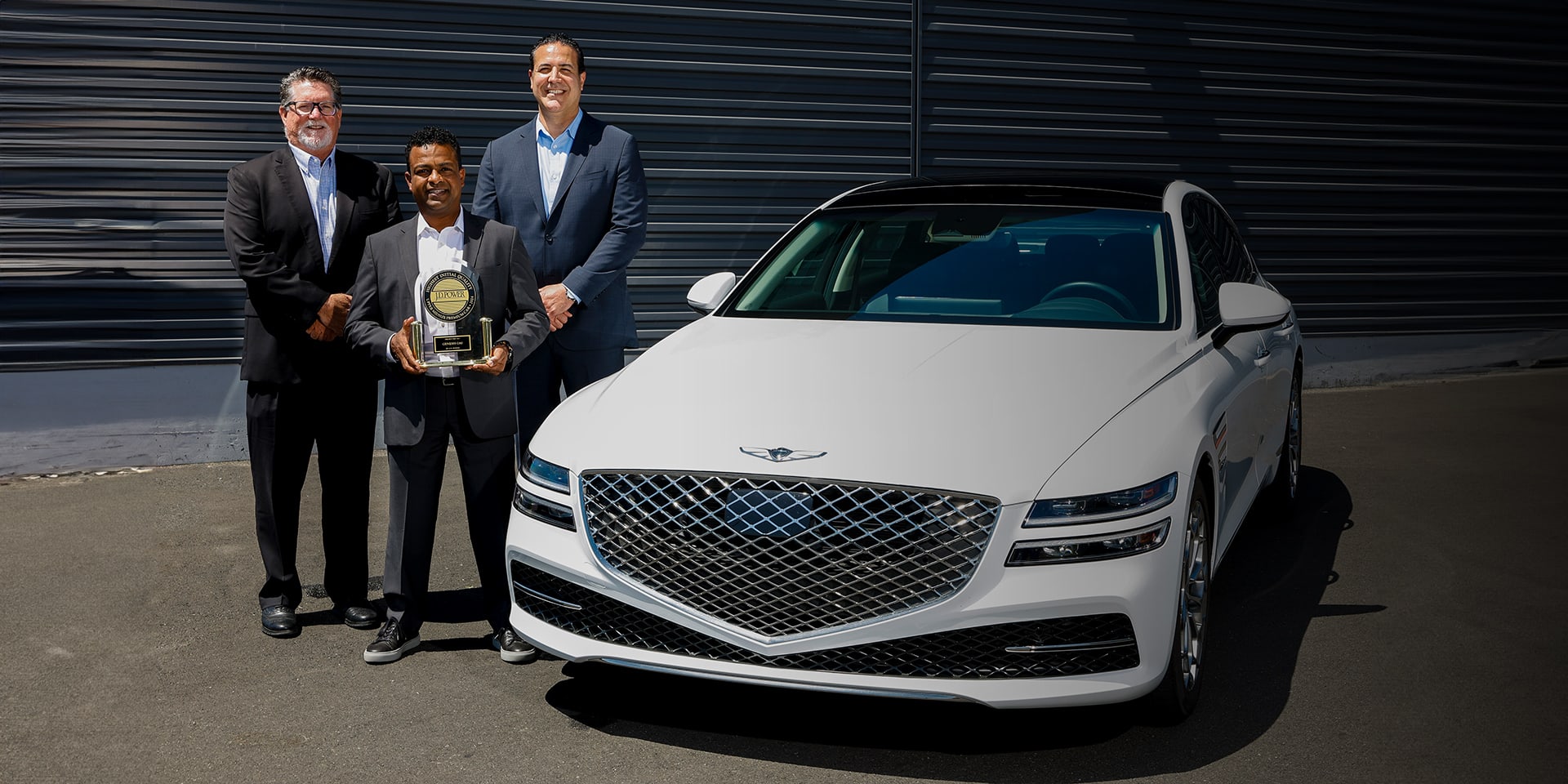 3 אנשים עומדים ליד ג'נסיס G80 עם פרס J.D. Power לשנת 2024