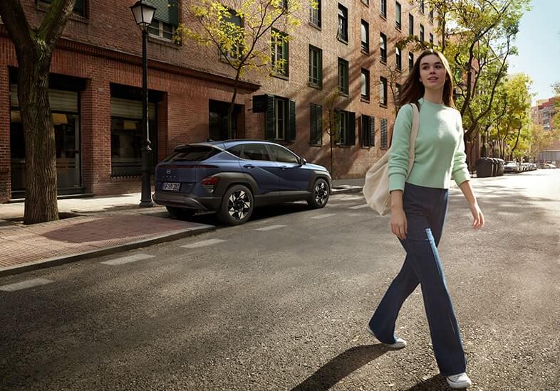 יונדאי קונה היברידית עומדת לצד בניין גדול ואישה עוברת את הכביש