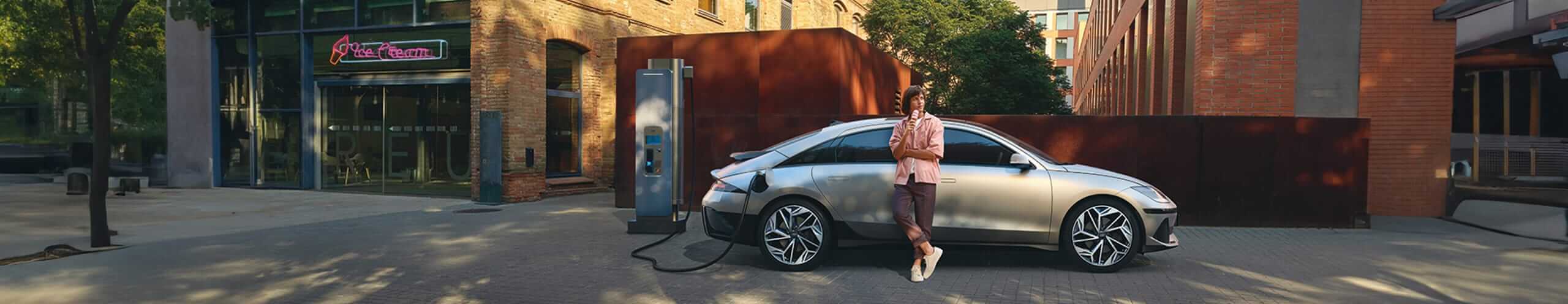 רכב מחובר לעמדת טעינה וגבר נשען על הרכב