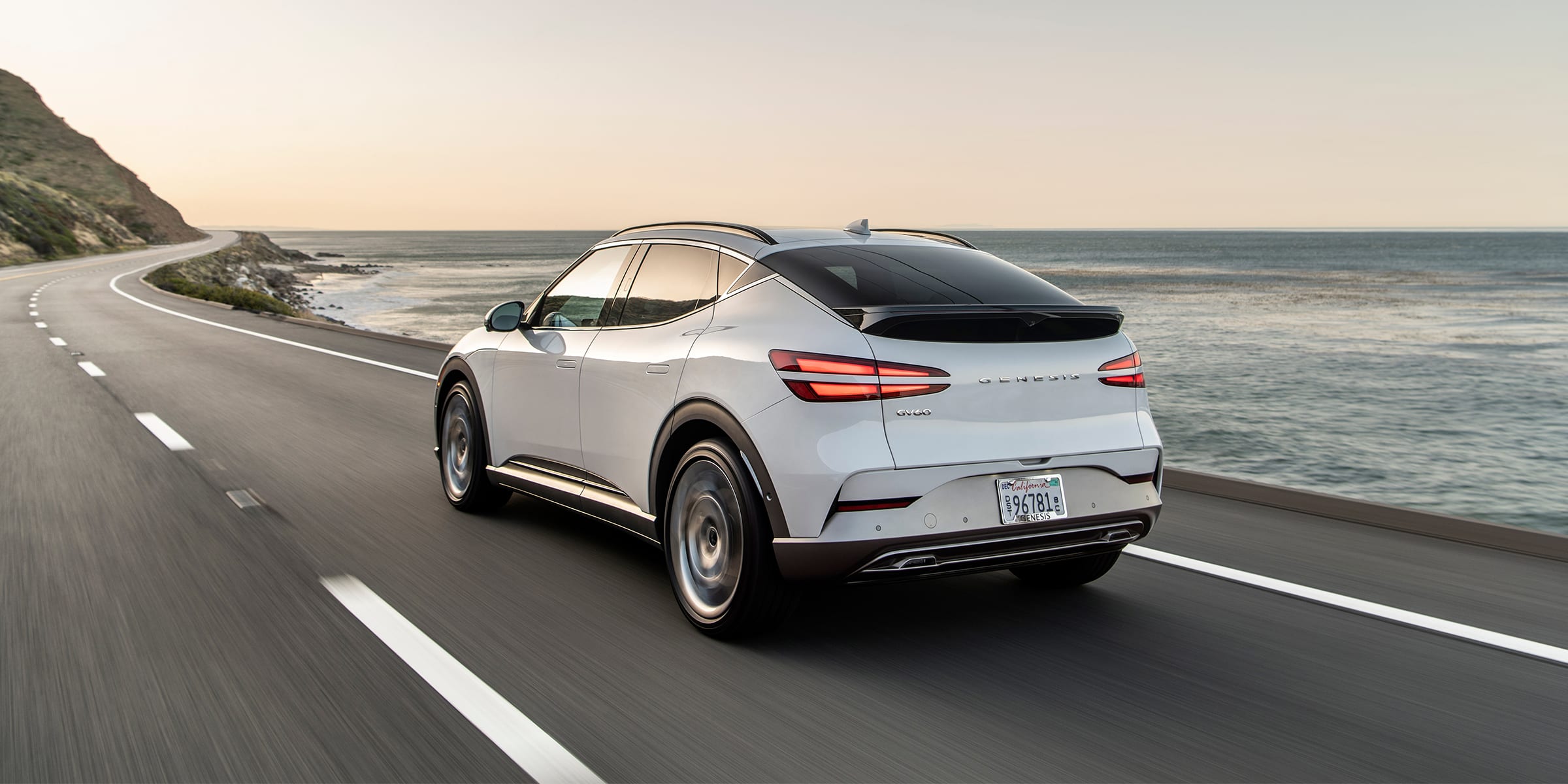 רכב חשמלי לבן נוסע בכביש ליד הים בשעת שקיעה.