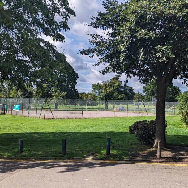 A fenced tennis court in the middle of an open lawn area.