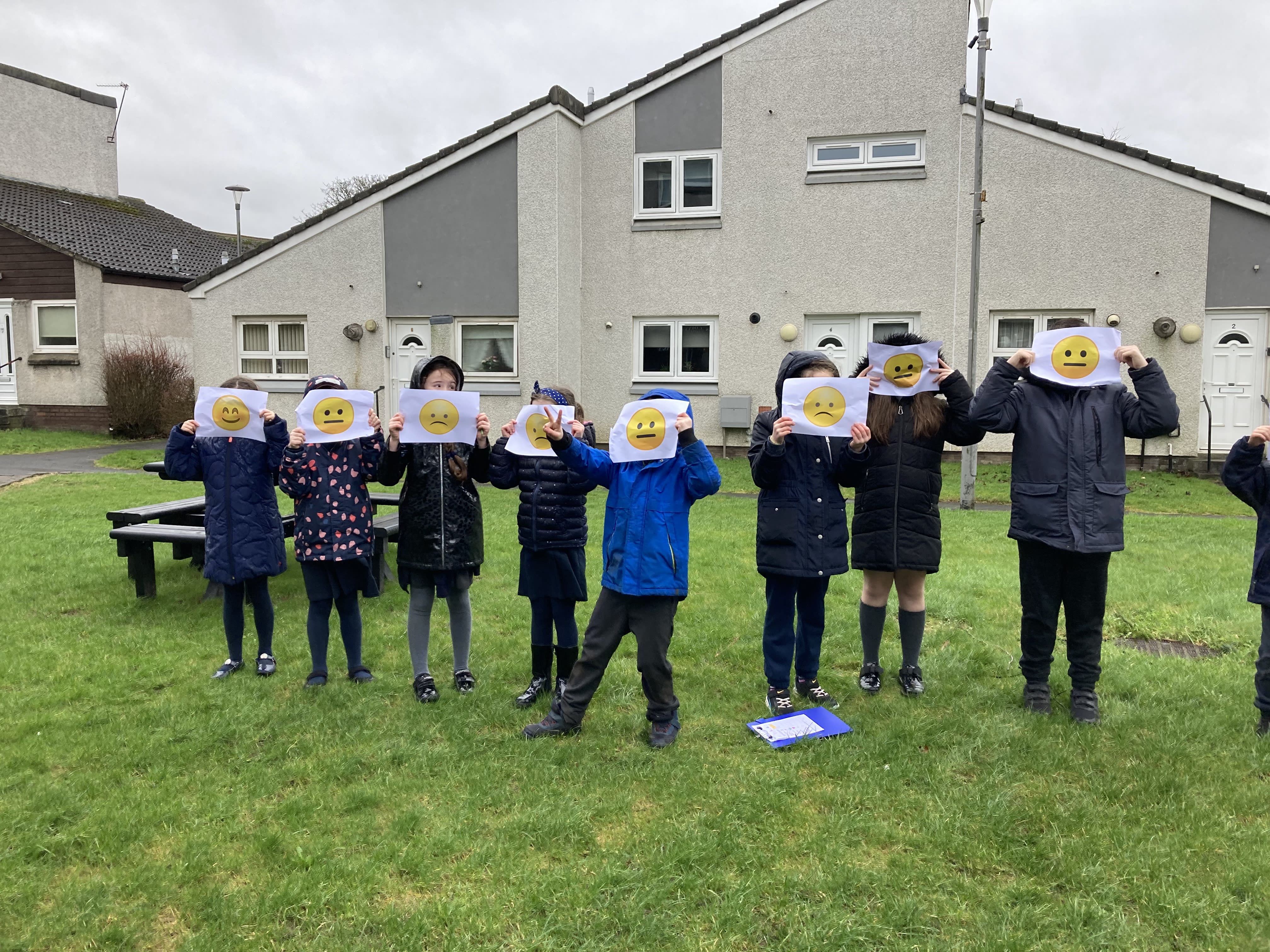 Children standing in a line on grass holding up paper with happy or sad faces