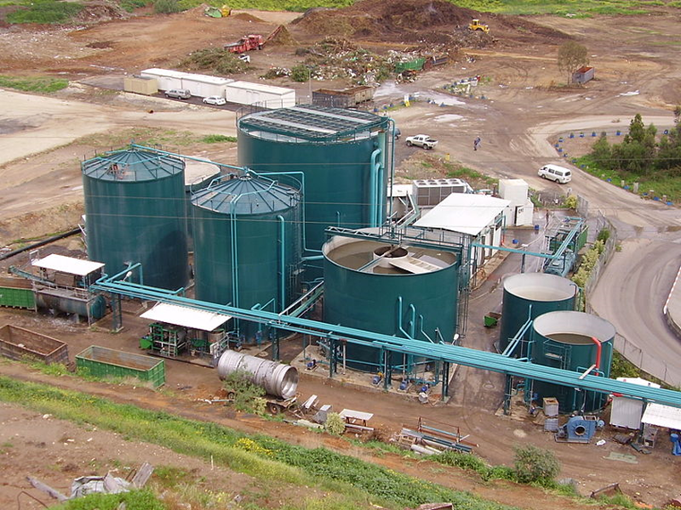 4 blue round metal structures around 30 meters tall are in an industrial landscape with a road around them.