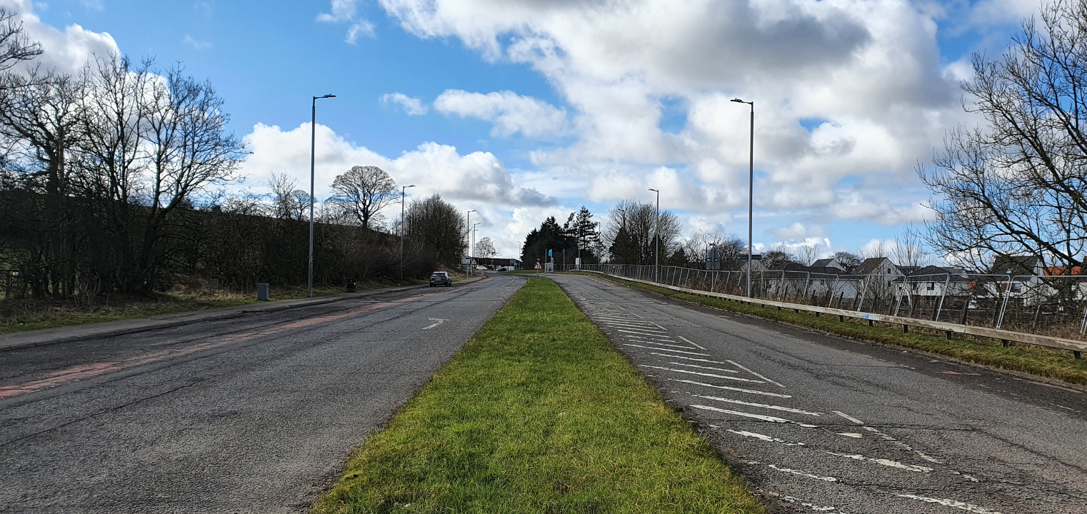 Road with grass central reservation, one lane in each direction, and advisory cycle lanes