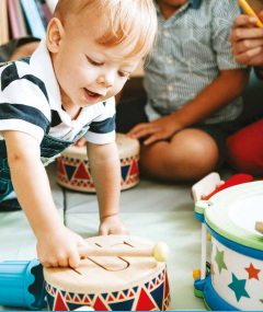 Young child in a white and blue striped polo shirt playing with a toy drum