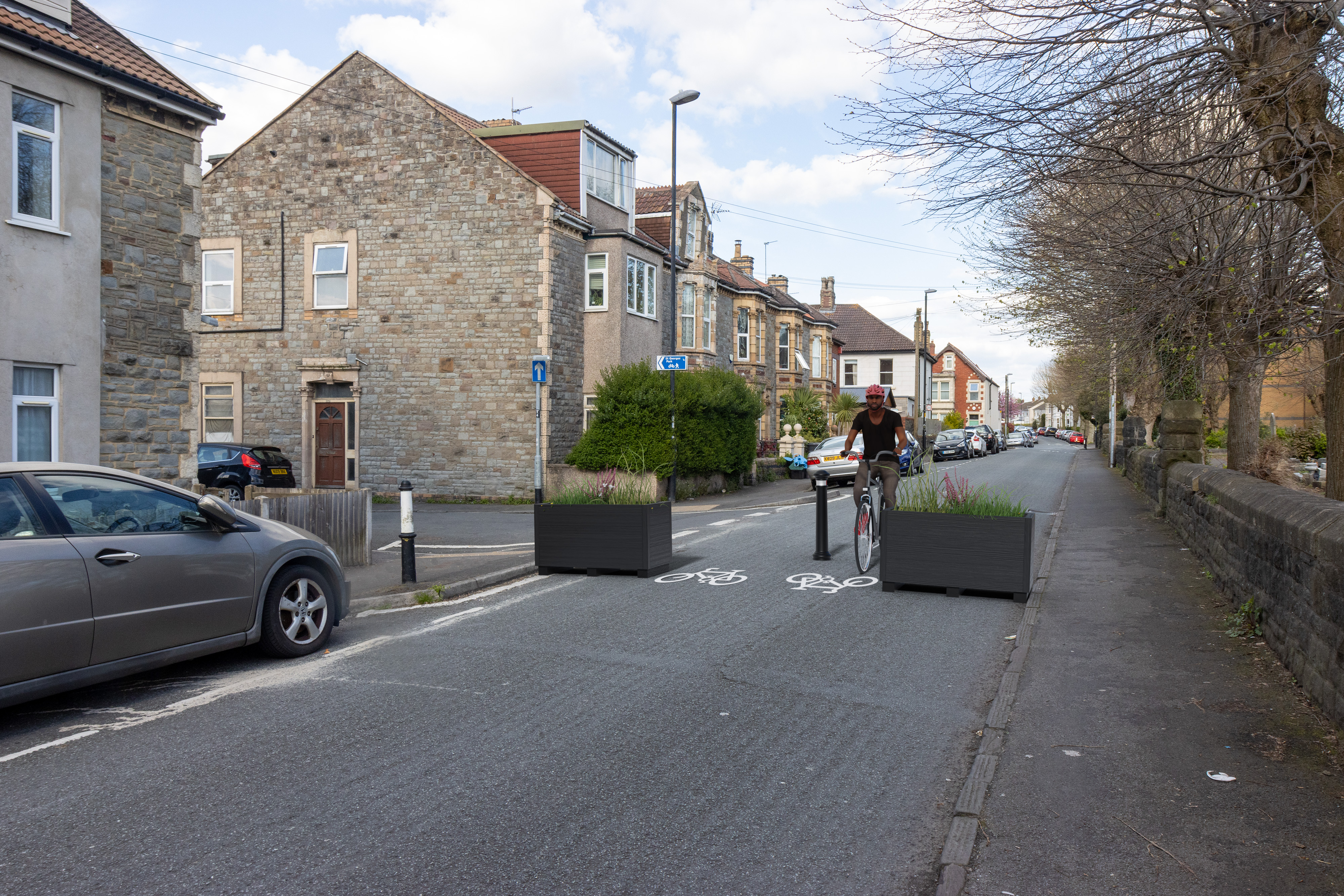 Two planters and a bollard in the middle of the road to stop vehicles passing through the pedestrian space. Cycle symbols to show where cycles will pass. 