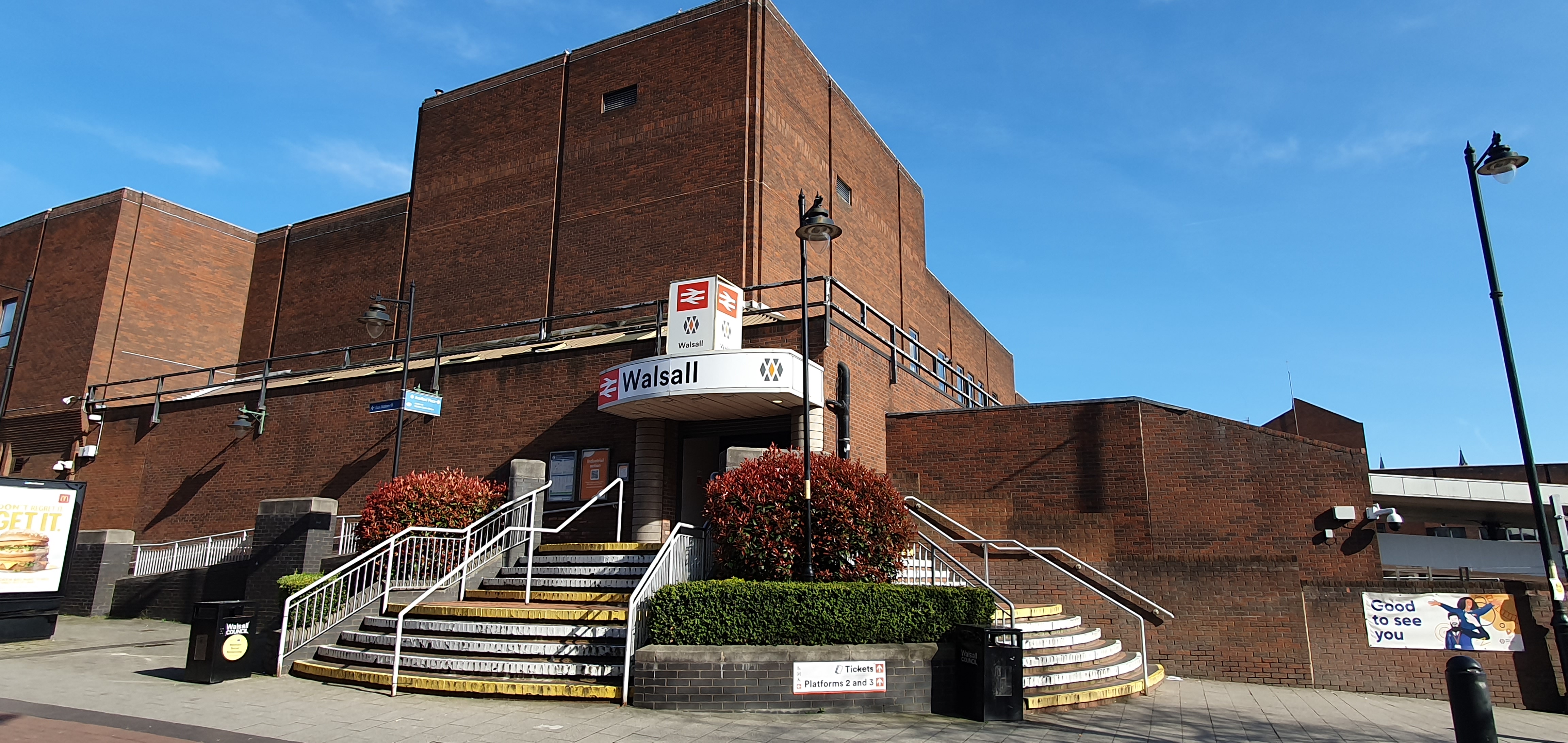 A red brick building with steps leading up towards a door, above which is a white sign that says Walsall with a red railway symbol.