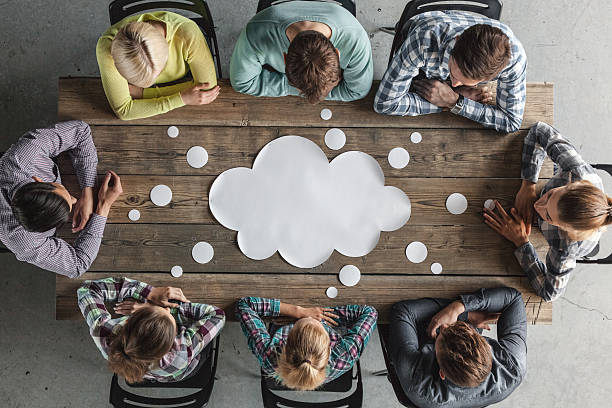 A group of people sitting around a table with a paper cloud

Description automatically generated