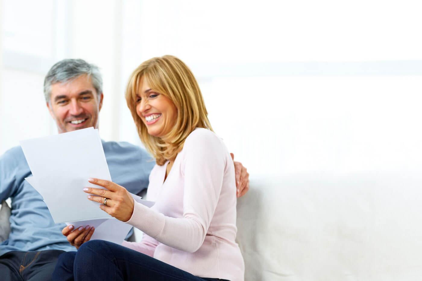 An older man and woman sitting down and smiling at their electricity bill