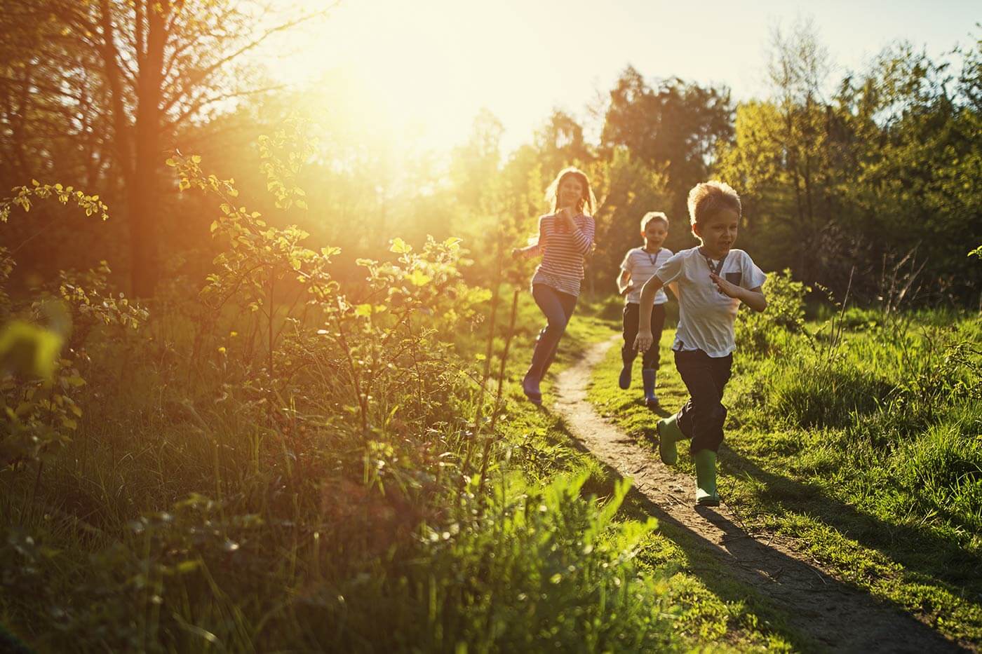 Three young children running along a forest trail