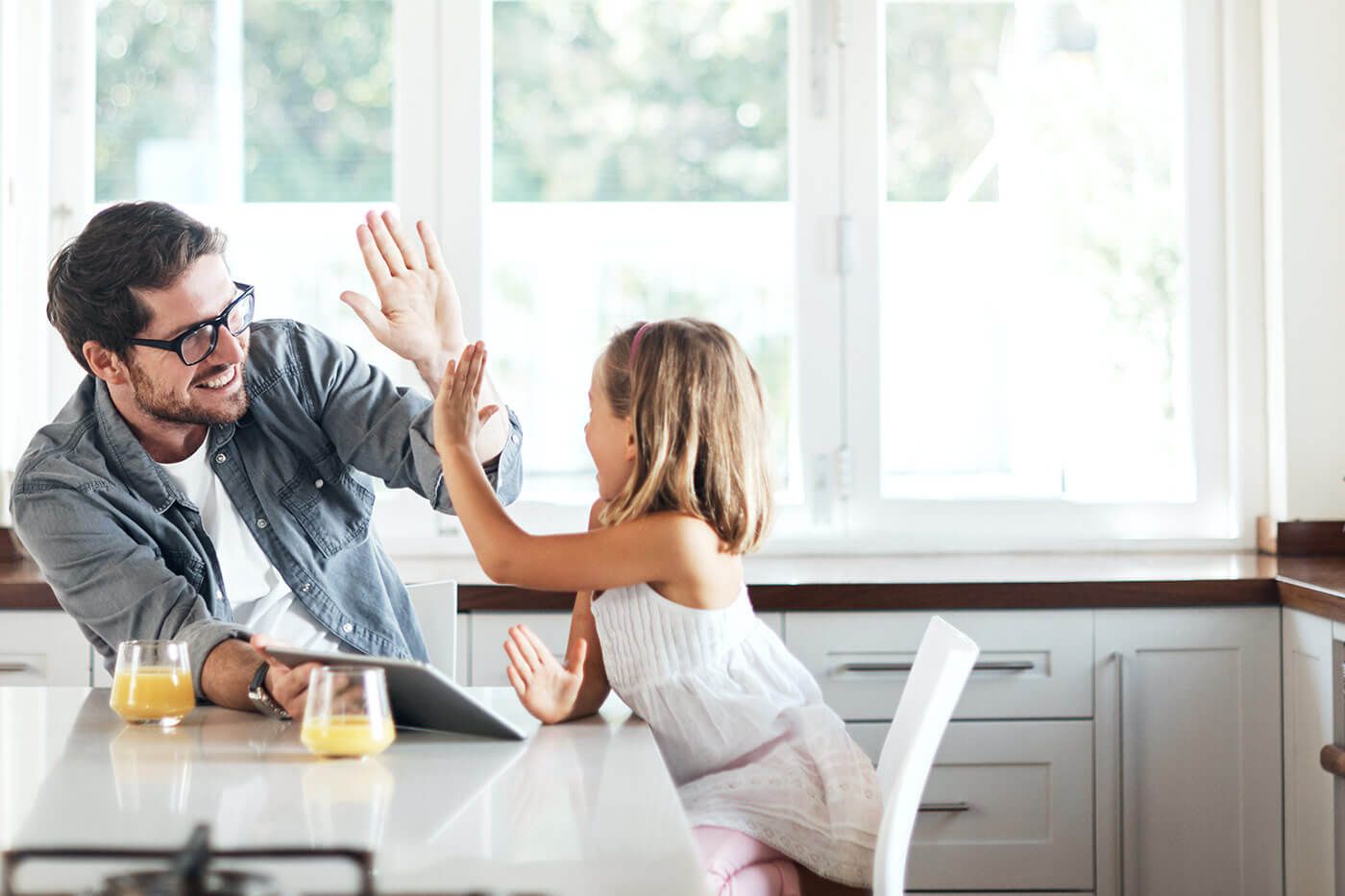 A dad giving his daughter a high-five in the kitchen while holding a tablet
